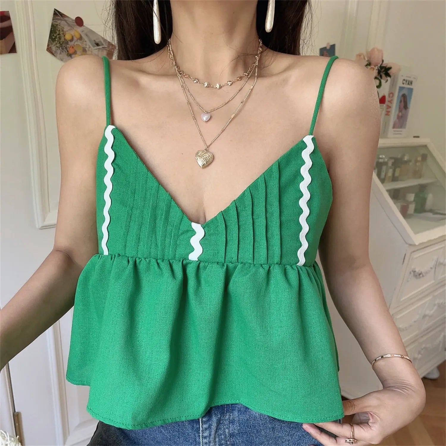 Lifestyle shot of model in the green wavy-edge peplum camisole top, holding a straw bag