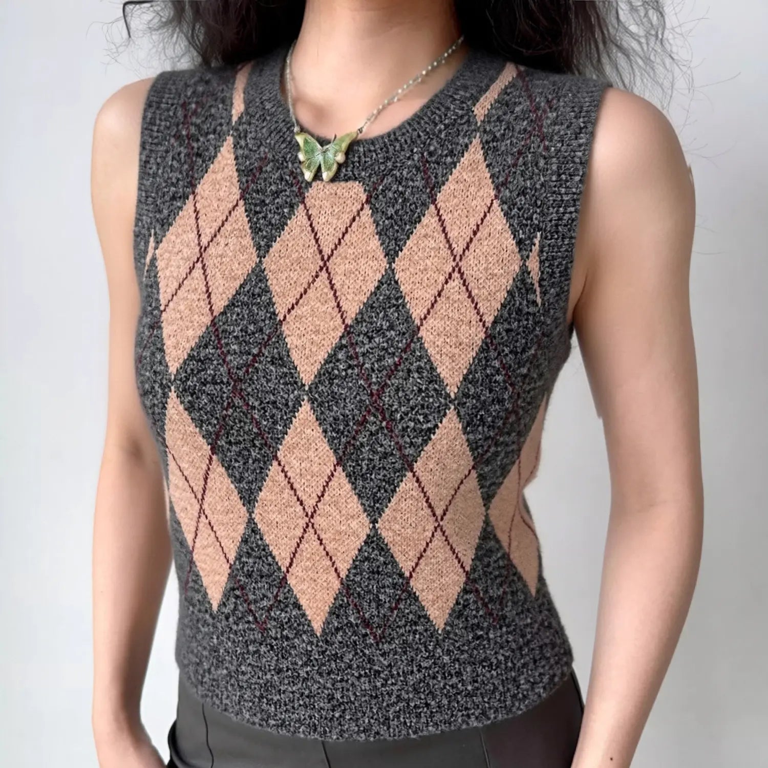Lifestyle wearing shot of grey and beige argyle print knit vest, paired with bottoms