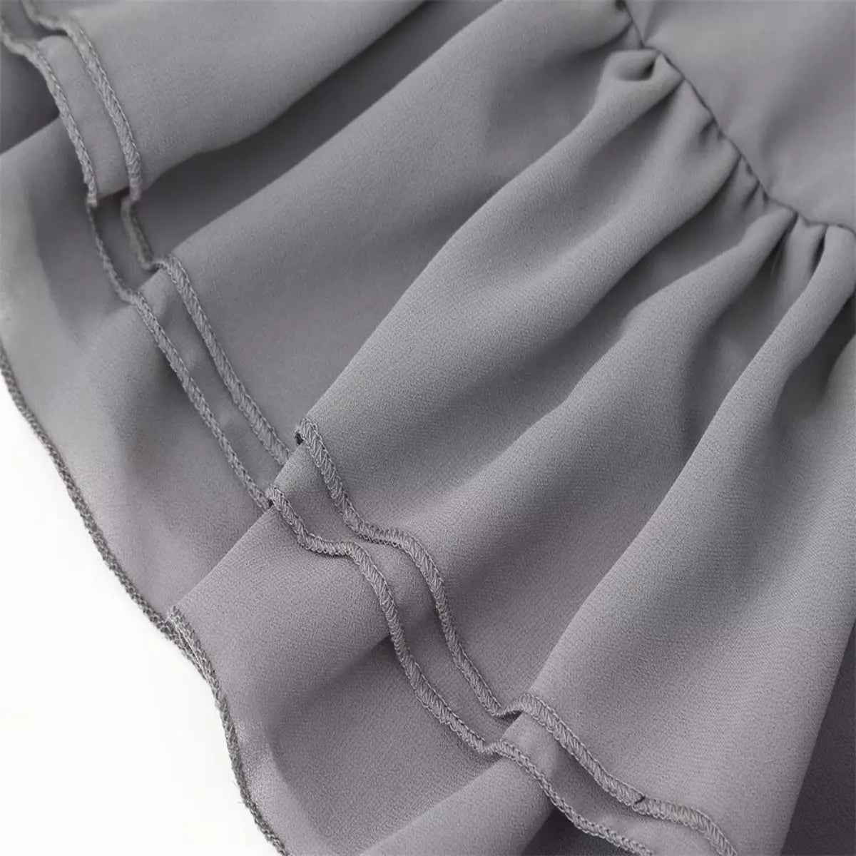 Hem view of the grey chiffon dress, showing the double-stitched edge and flowy ruffled fabric