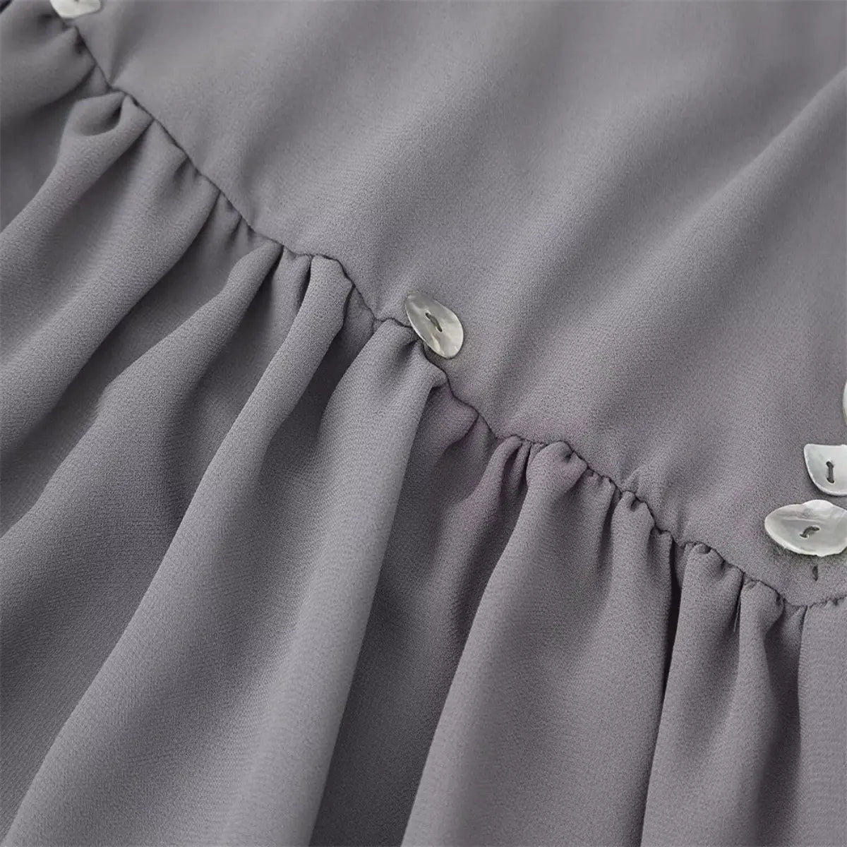 Close-up of the tiered seam on the grey chiffon dress, showing the shell buttons and gathered ruffle detail