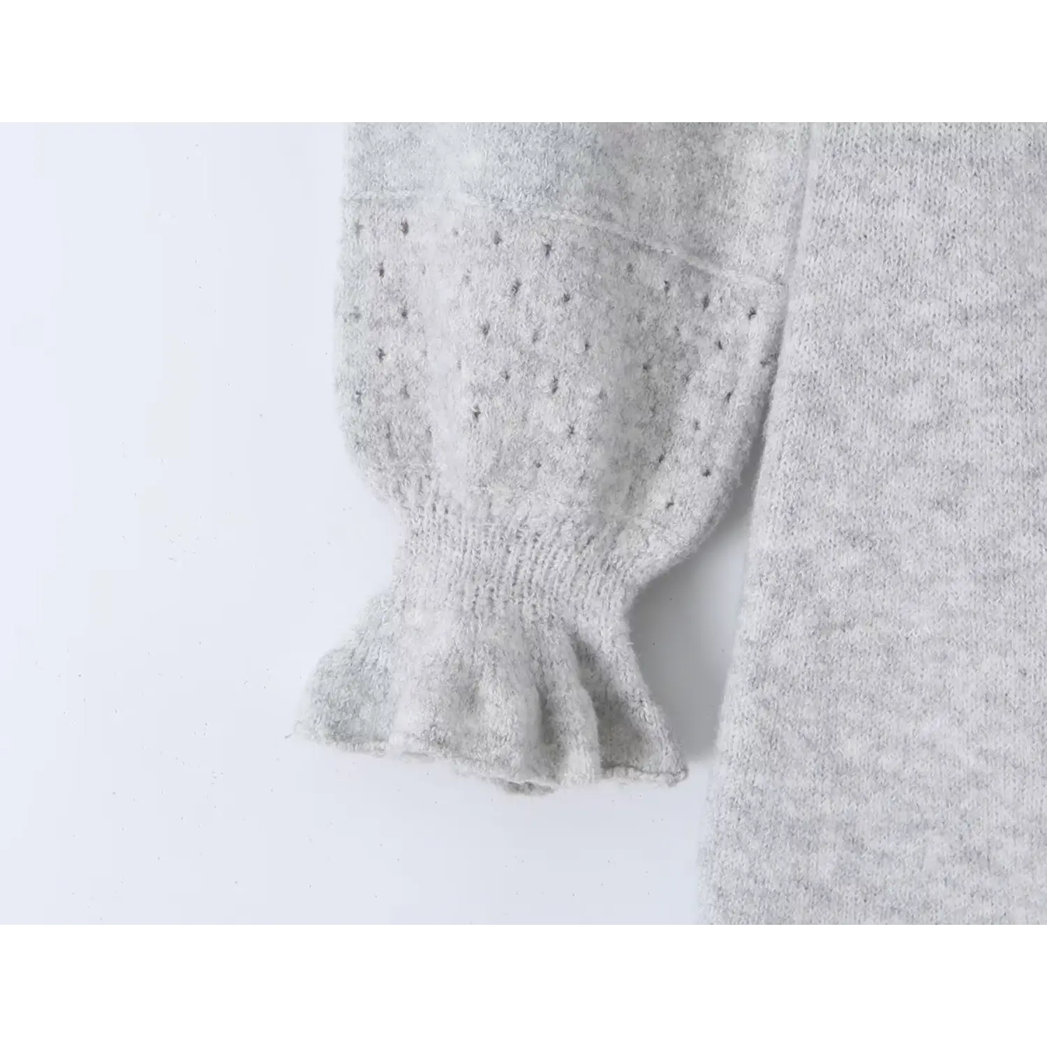 Close up of long bubble sleeve hollow knit panel and flared ruffle cuff on light gray sweater dress