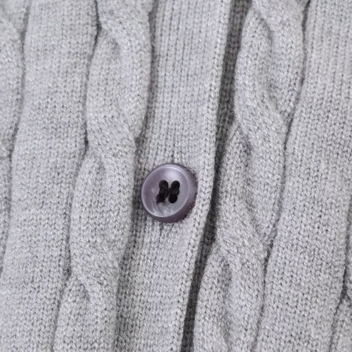 Close-up of the grey cable knit vest's purple button, showing the twisted stitch pattern
