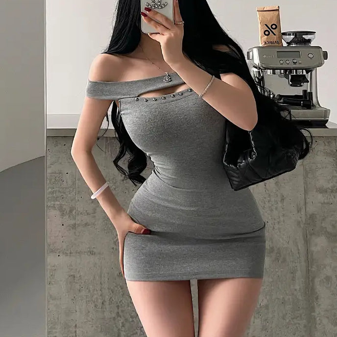 A woman taking a mirror selfie while wearing a grey ribbed off-shoulder mini dress with stud details, styled with a headband and a black bag.