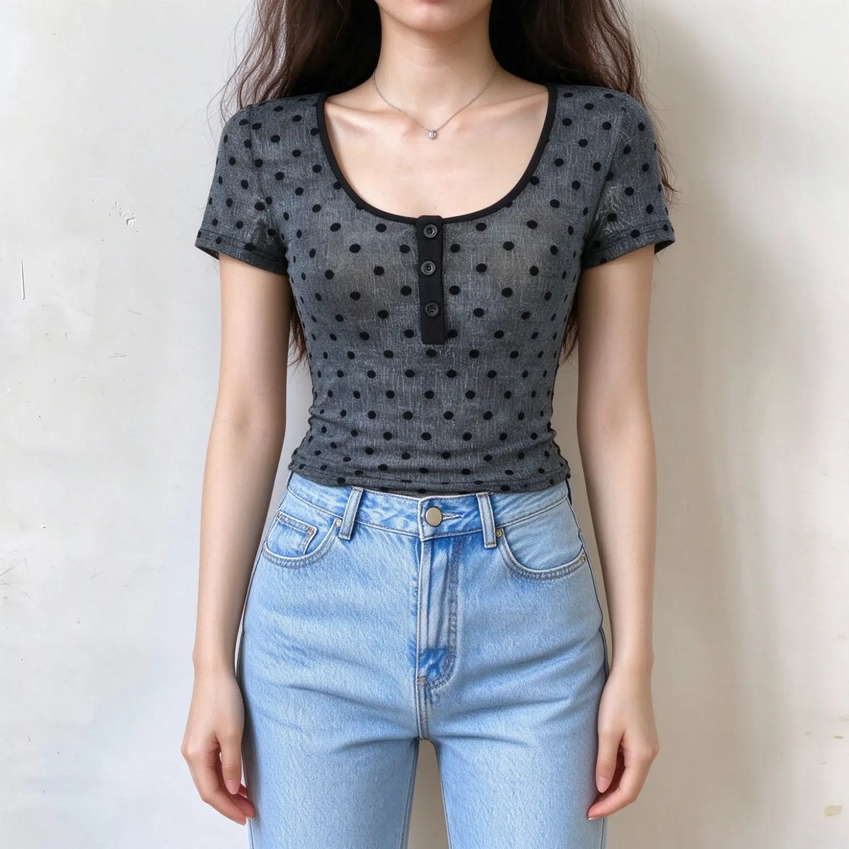 Model wearing grey polka dot short sleeve mesh top, scoop neck black binding, henley button front, semi-sheer fabric, slim fit with light blue jeans against plain white background
