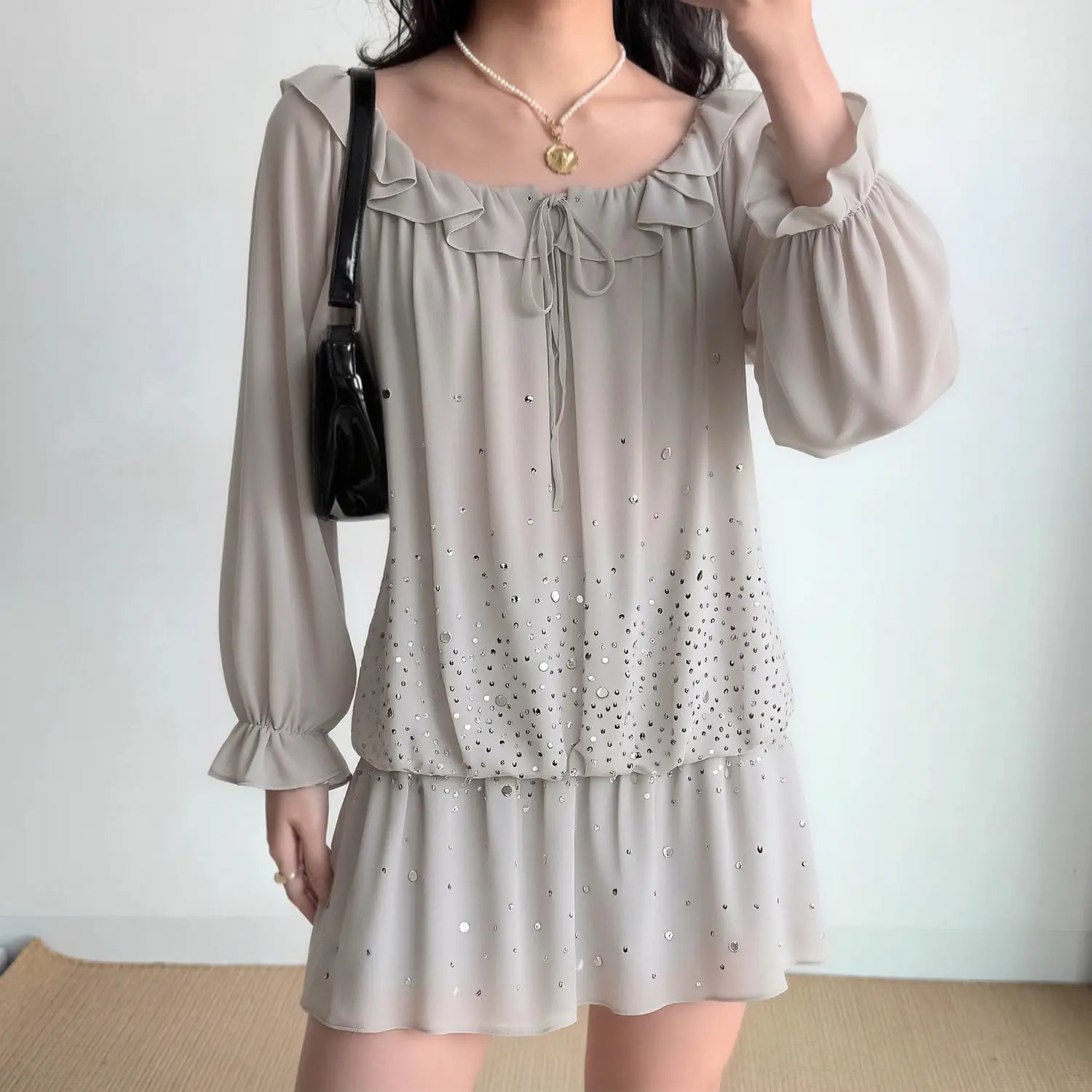 Model wearing grey off‑shoulder sequin mini dress, ruffle neckline, drawstring tie, long ruffle‑cuff balloon sleeves, tiered flowy skirt