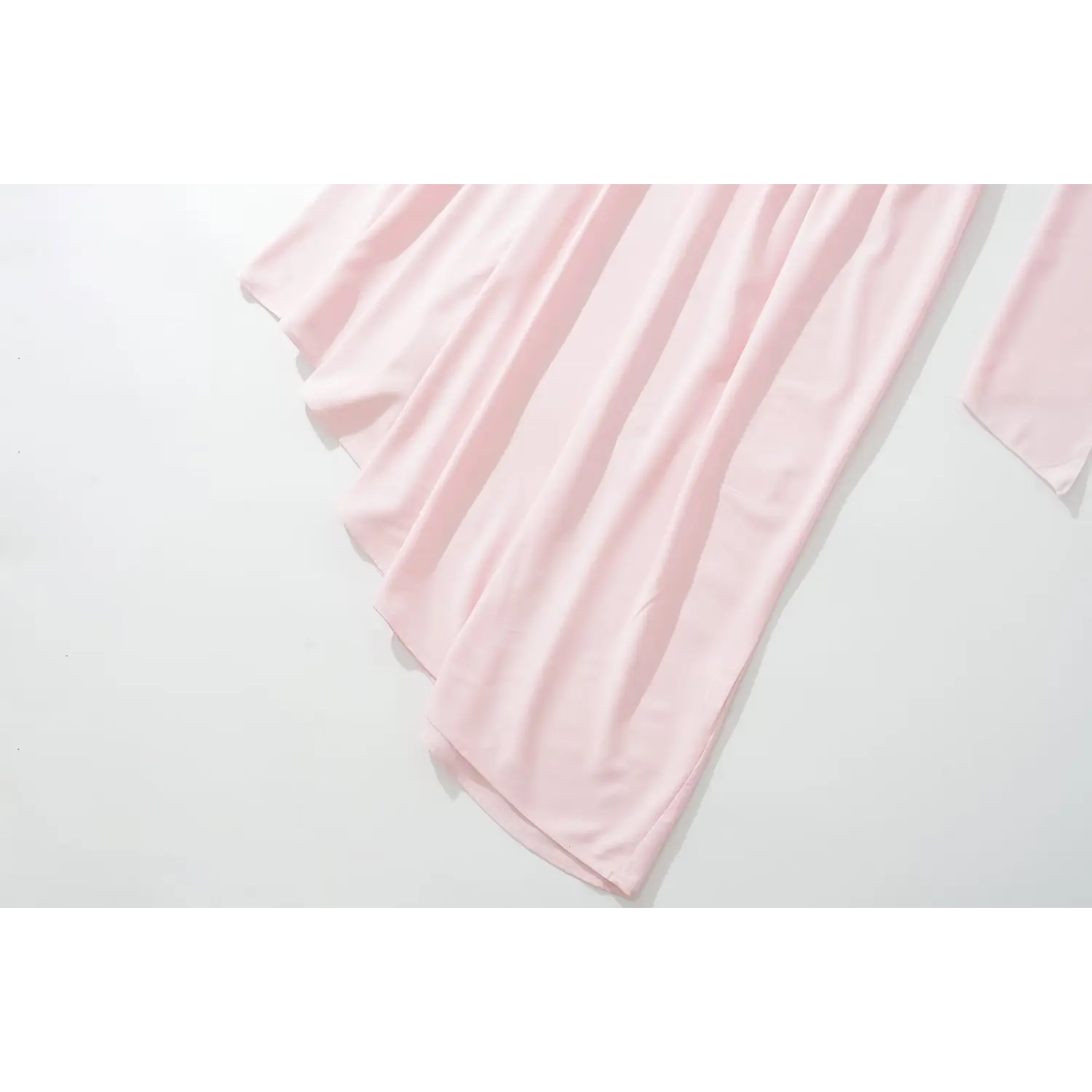 Flat lay partial shot of blush pink satin maxi dress skirt, soft cascading draped fabric with asymmetrical uneven hem and smooth matte woven texture