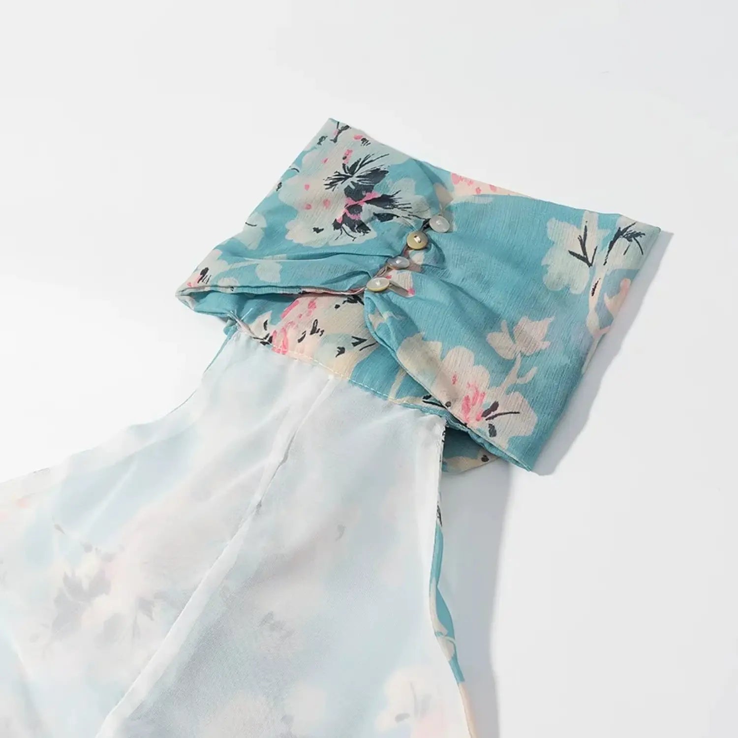 Close‑up of halter back neck, decorative pearl buttons on ruffled blue floral chiffon fabric