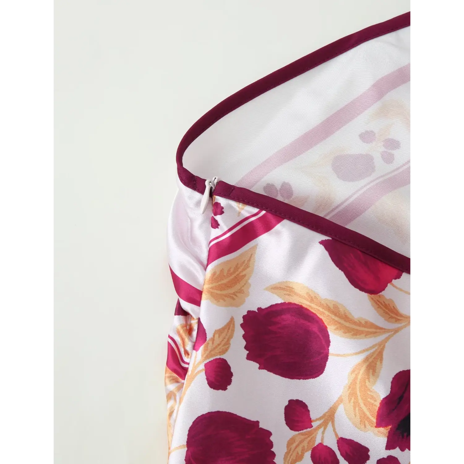Close‑up of dress side seam, burgundy piping trim, hidden side zipper and satin floral print fabric