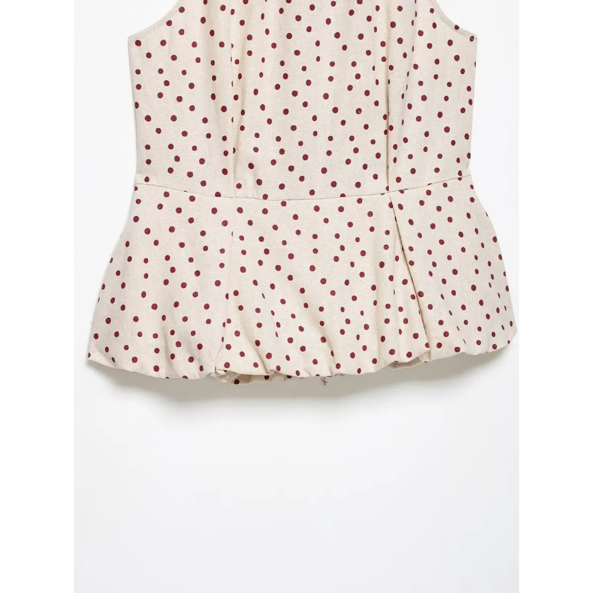 Close-up of the peplum hem on a beige polka-dot halter top, showing the flared, bubble hem and linen-like fabric texture.