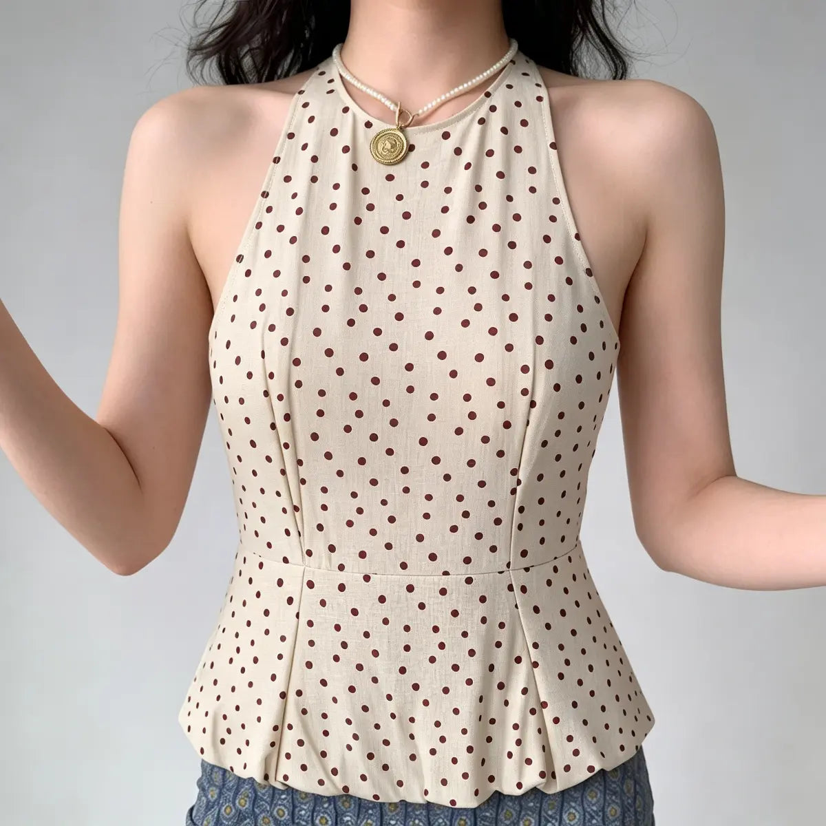 Model with arms raised, showcasing the fit of a beige halter peplum top with red polka dots, emphasizing the sleeveless design and structured silhouette.
