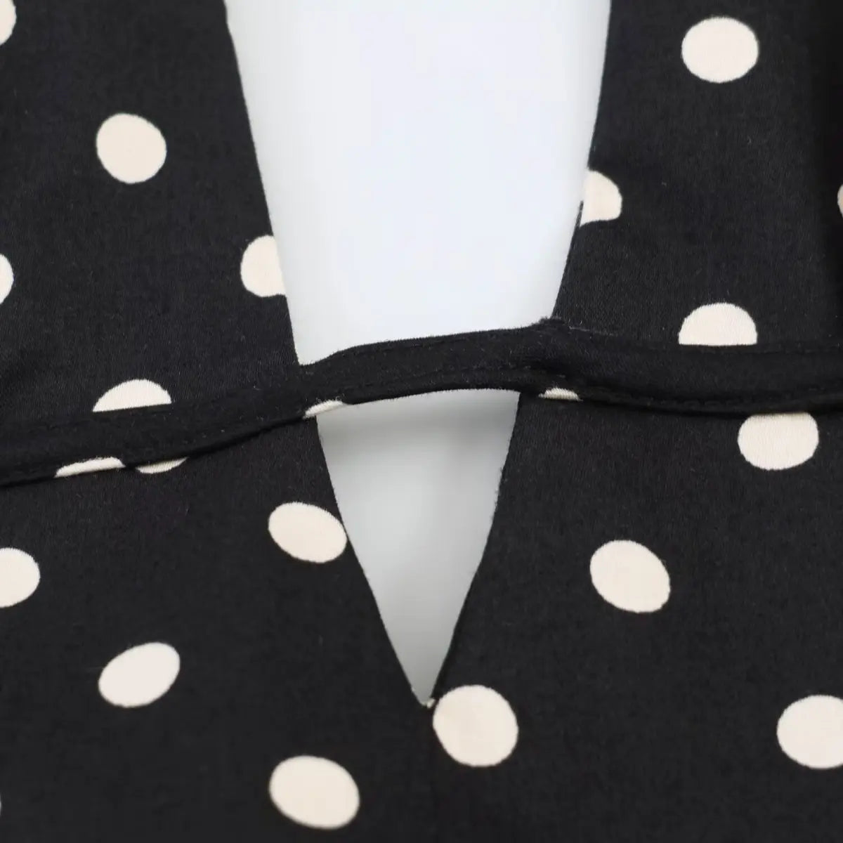 Close-up of the V-neck cutout detail on black polka dot halter dress, showing fabric and stitching.