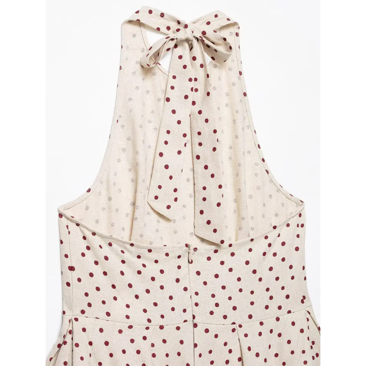 Close-up of the back tie closure on a beige halter top with red polka dots, showing the fabric bow and cutout detail.