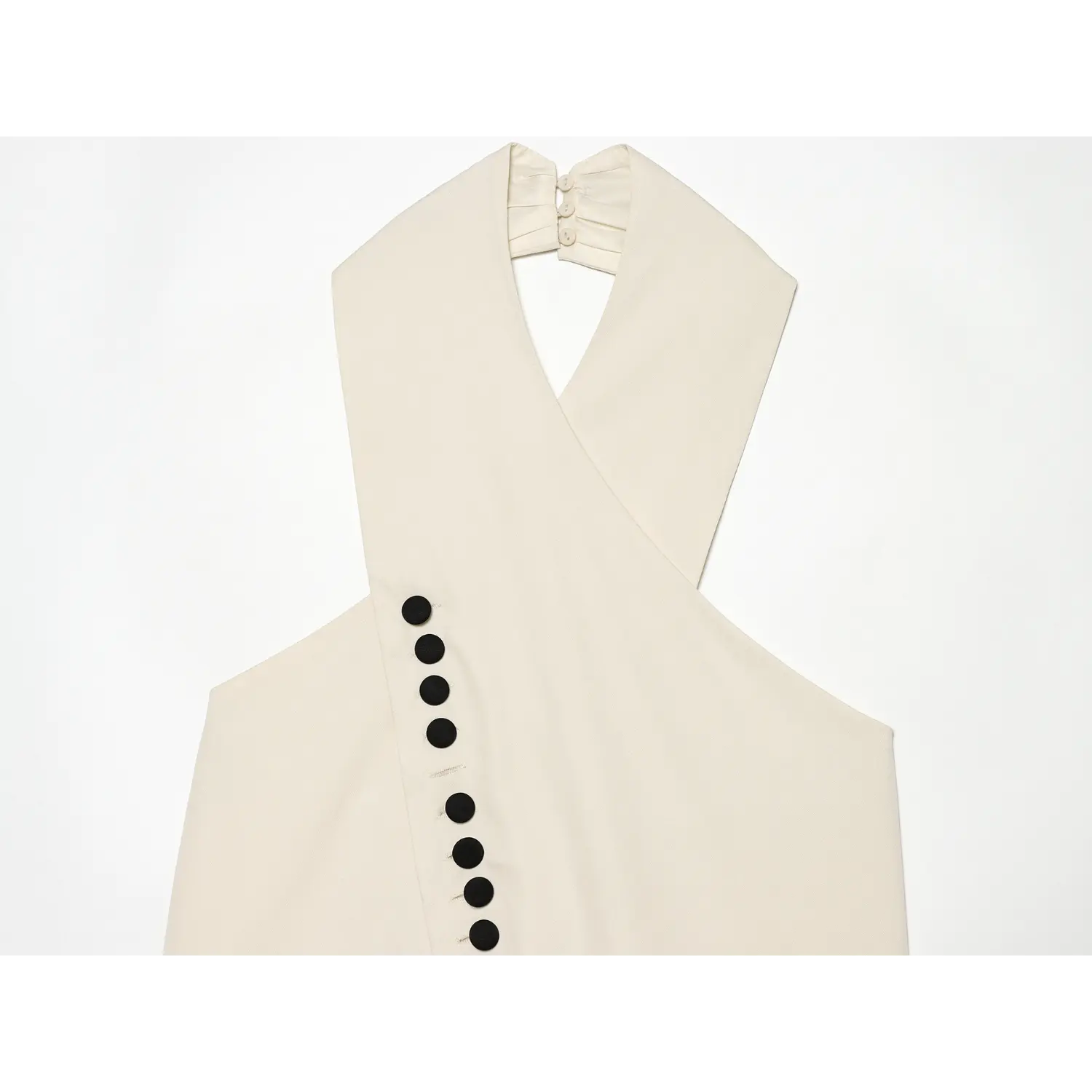 Close-up of wrap cross neck and black decorative buttons on cream halter top
