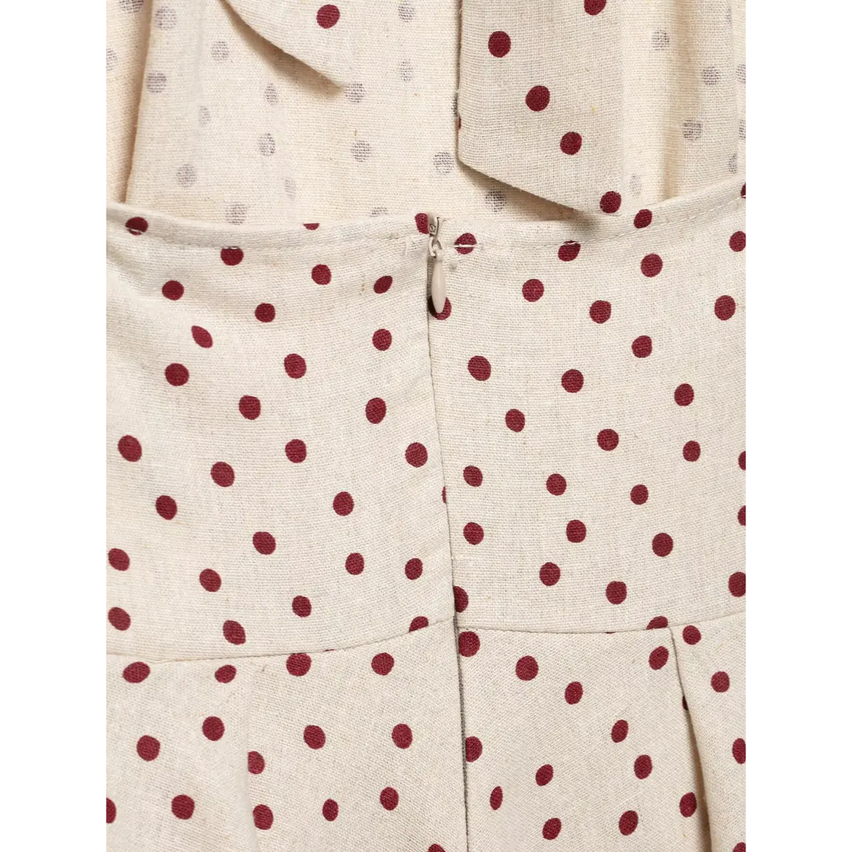 Close-up of the zipper and seam on the back of a beige polka-dot halter top, showing the construction and fabric texture.