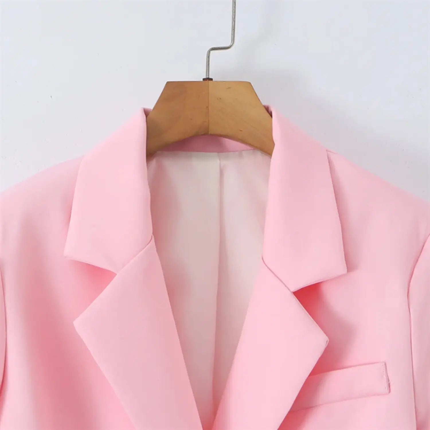 Hanger close-up of notched lapel collar, open front neckline, light pink inner lining, tailored collar roll, smooth suiting texture