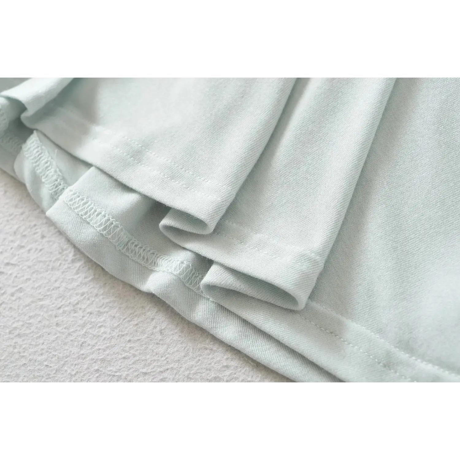 Macro view of skirt hem stitching on haze blue fit and flare mini dress, fine stretch seam