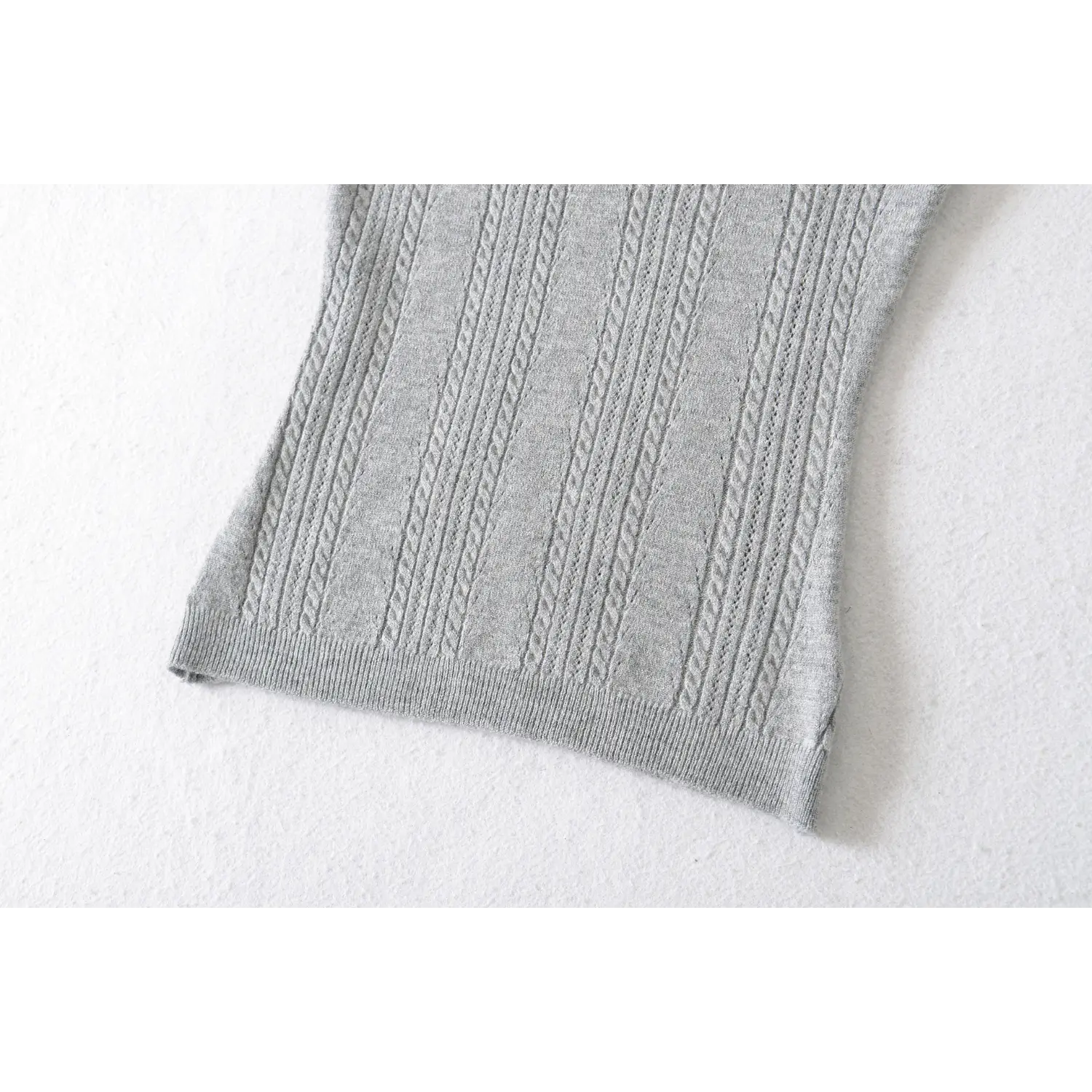 Close up detail of ribbed bottom hem on gray cable knit cropped top, stretch rib trim twist knit fabric