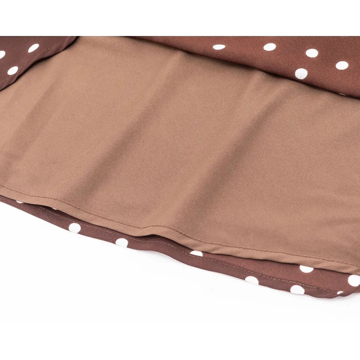 Close-up of the hem on a brown and white polka dot dress, revealing the smooth lining and finished edge stitching.