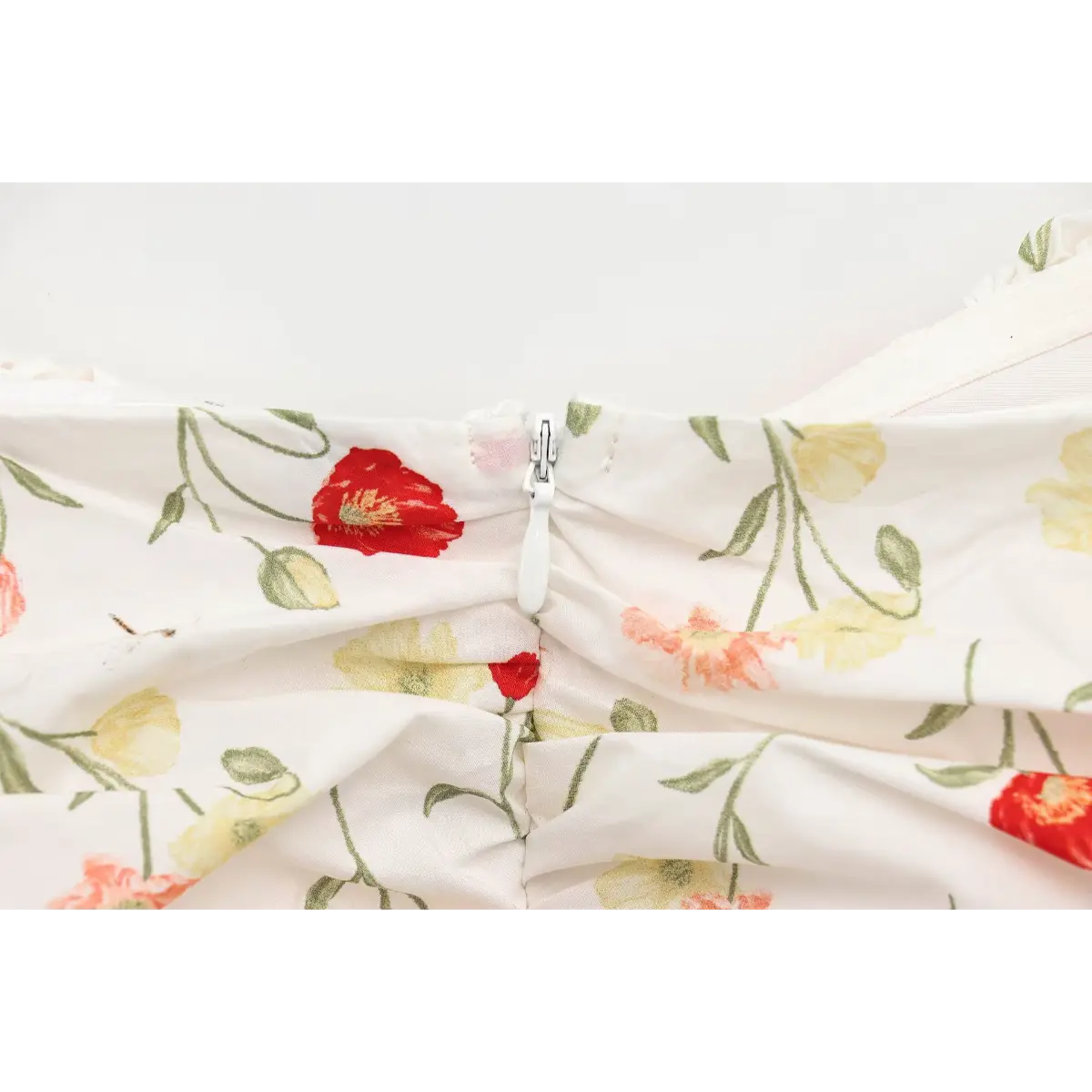 Close-up of the hidden center-back zipper on a white poppy-print dress, showing the fabric-covered pull.
