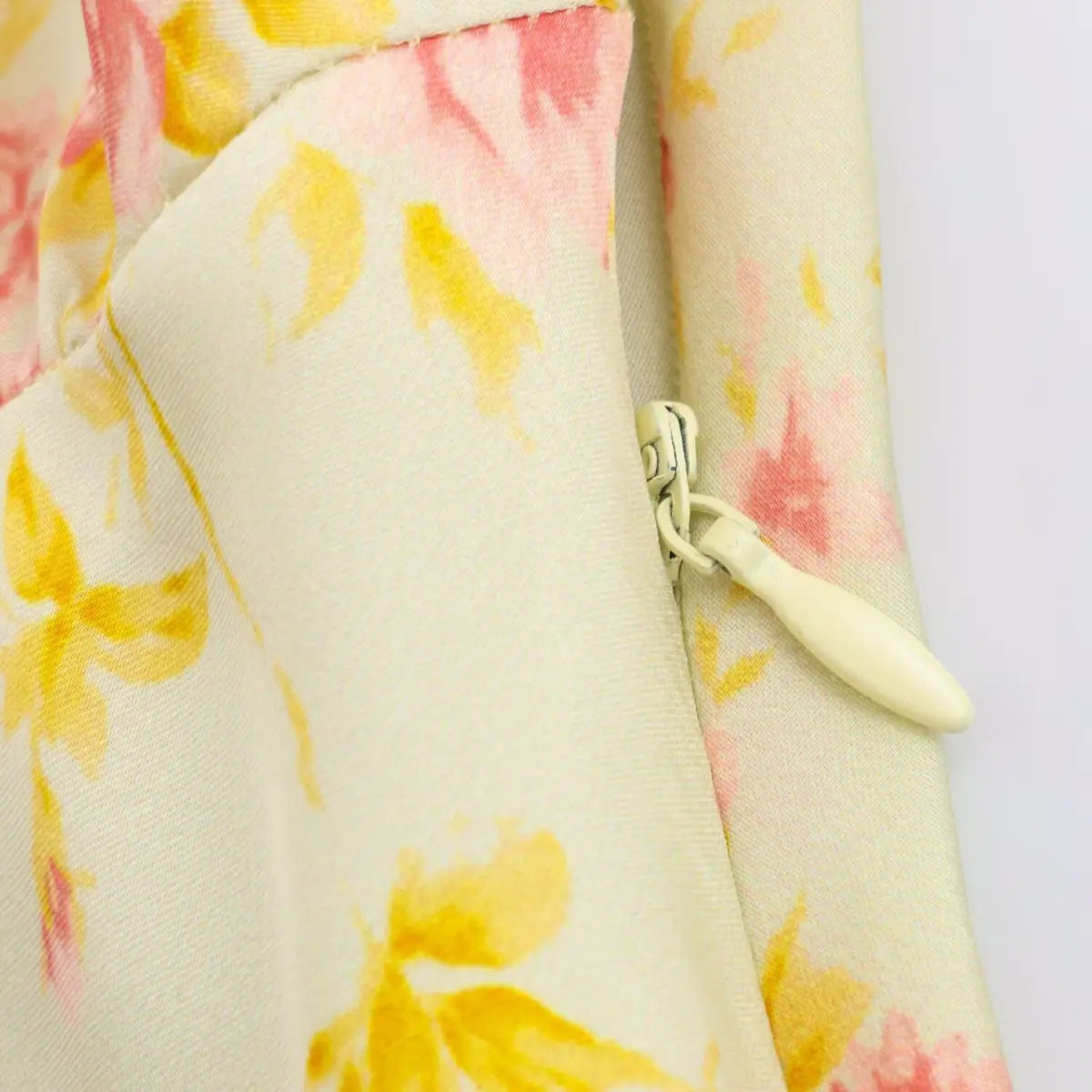 Close-up of the hidden side zipper on a pale yellow floral dress, showing the fabric-covered pull.