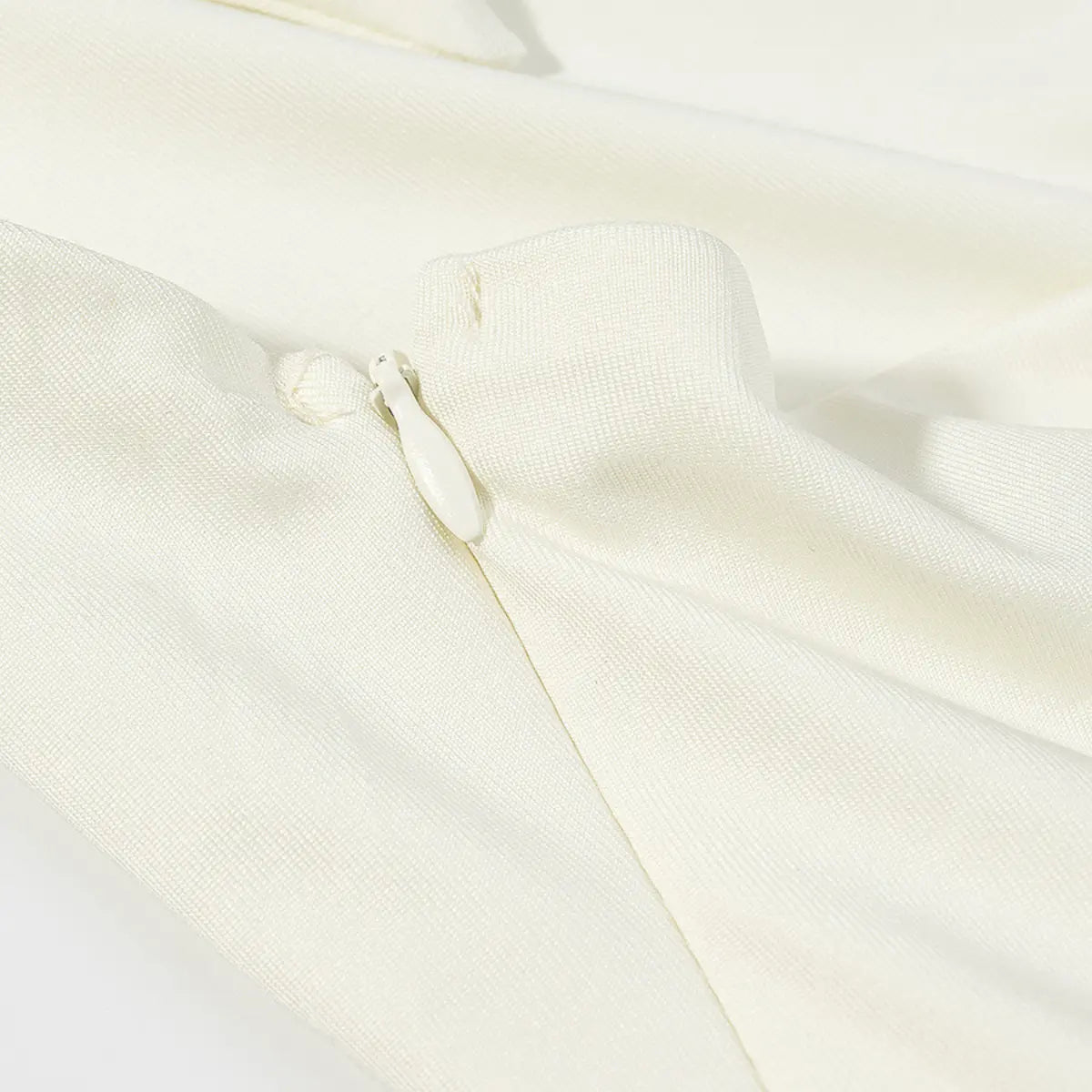 Close-up of the hidden zipper on a cream halter dress, showing the fabric-covered pull and seamless stitching.