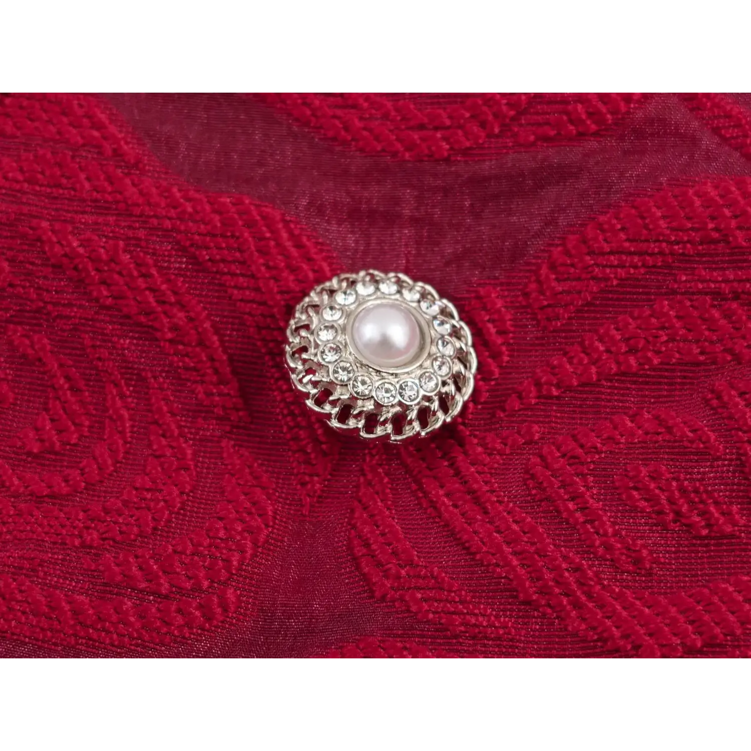 Macro shot ornate circular button, hollow silver frame encrusted with small rhinestones, central large smooth faux pearl