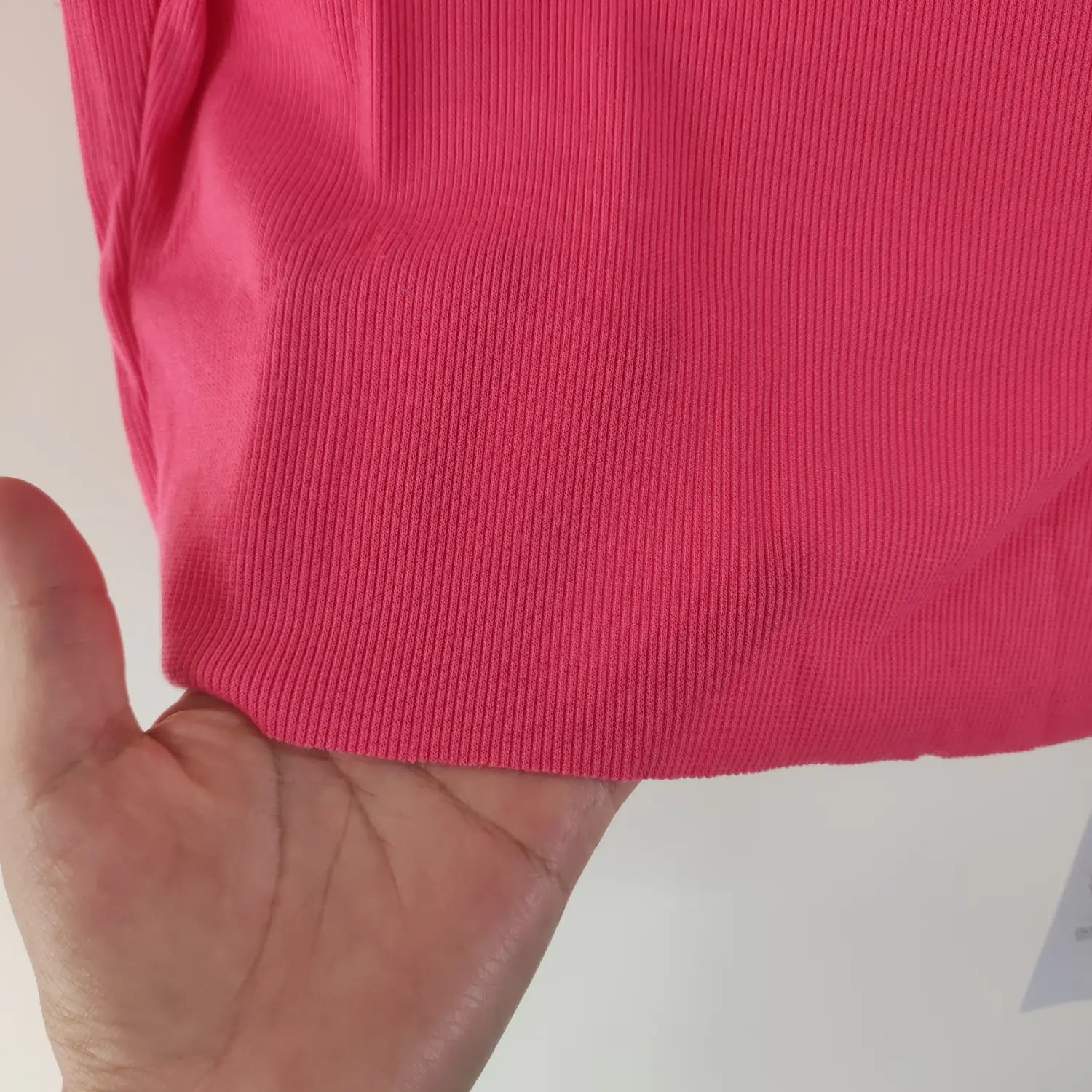 Hand hold close‑up show stretch rib fabric and raw hem of hot pink mock neck crop top