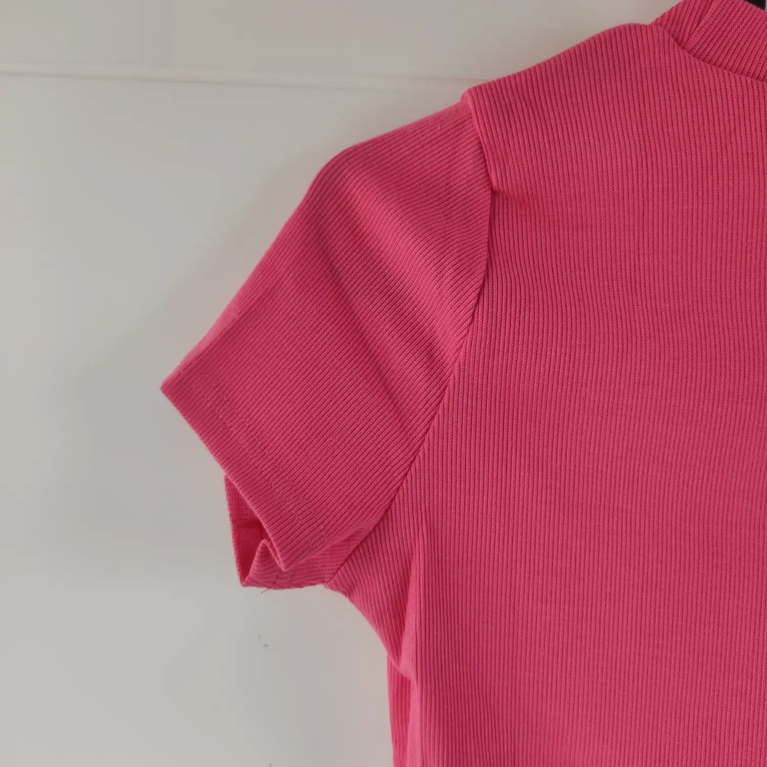 Close‑up shoulder and short sleeve seam detail of hot pink ribbed mock neck crop top