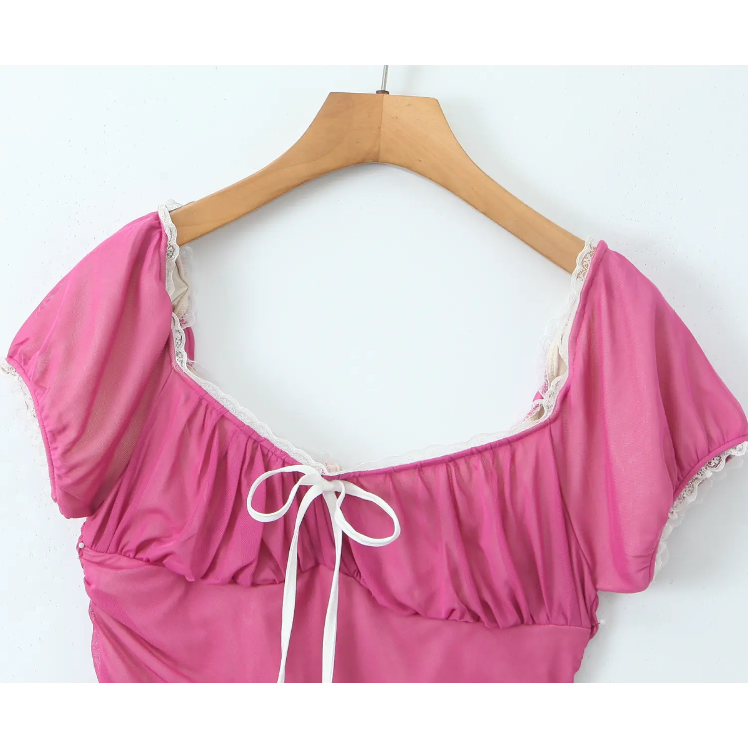 Close‑up of hot pink mesh dress square neckline, white lace edging, bust ruched detail and white front bow tie