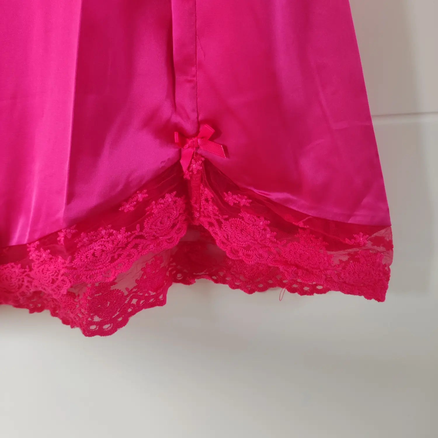 Close‑up front hem slit with small satin bow and scalloped lace trim