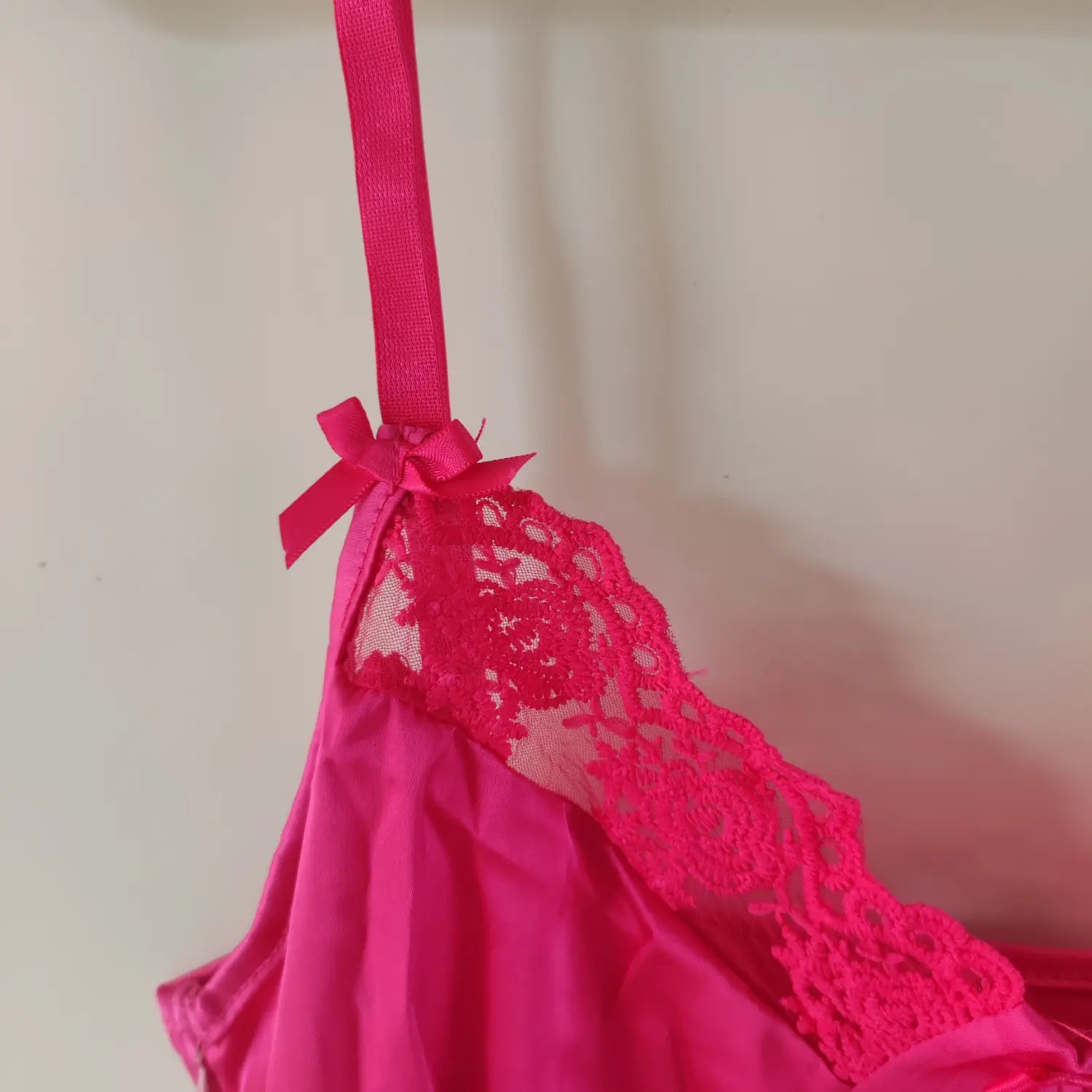 Close‑up shoulder strap, satin bow and floral lace neckline detail hot pink slip dress