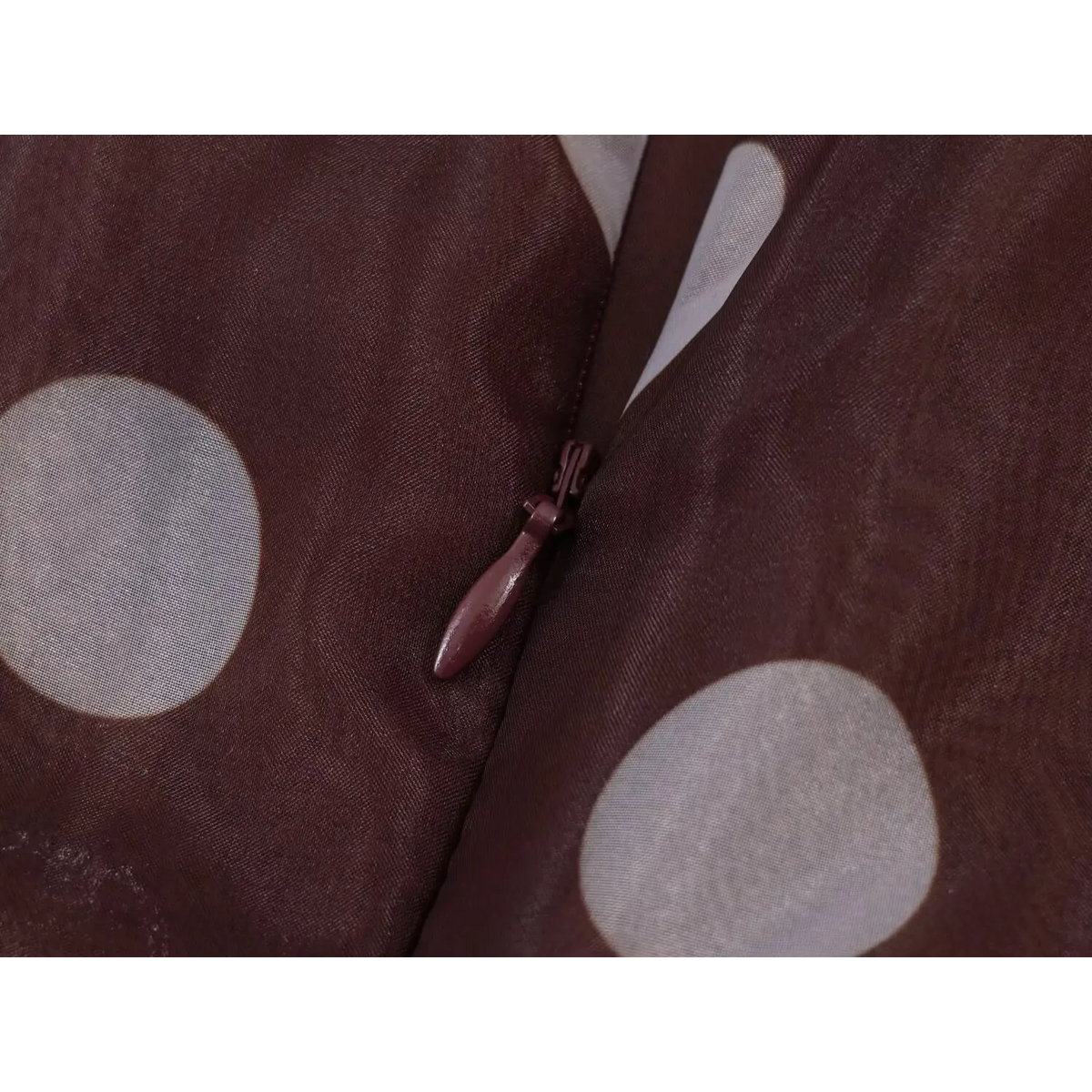 Close-up of brown invisible back zipper on sheer brown fabric with large white polka dots