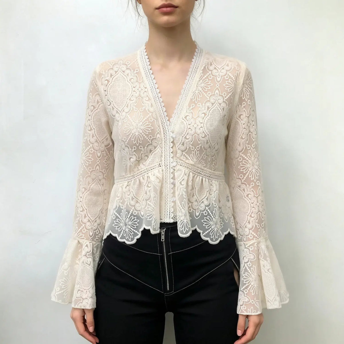 Model wearing ivory lace bell sleeve peplum top with black trousers