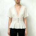 Model wearing ivory lace trimmed V neck peplum top with black trousers