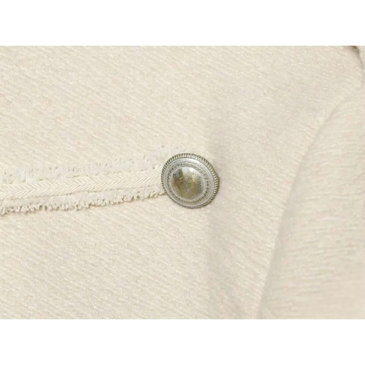 Close-up of metal button and braided trim on ivory military jacket