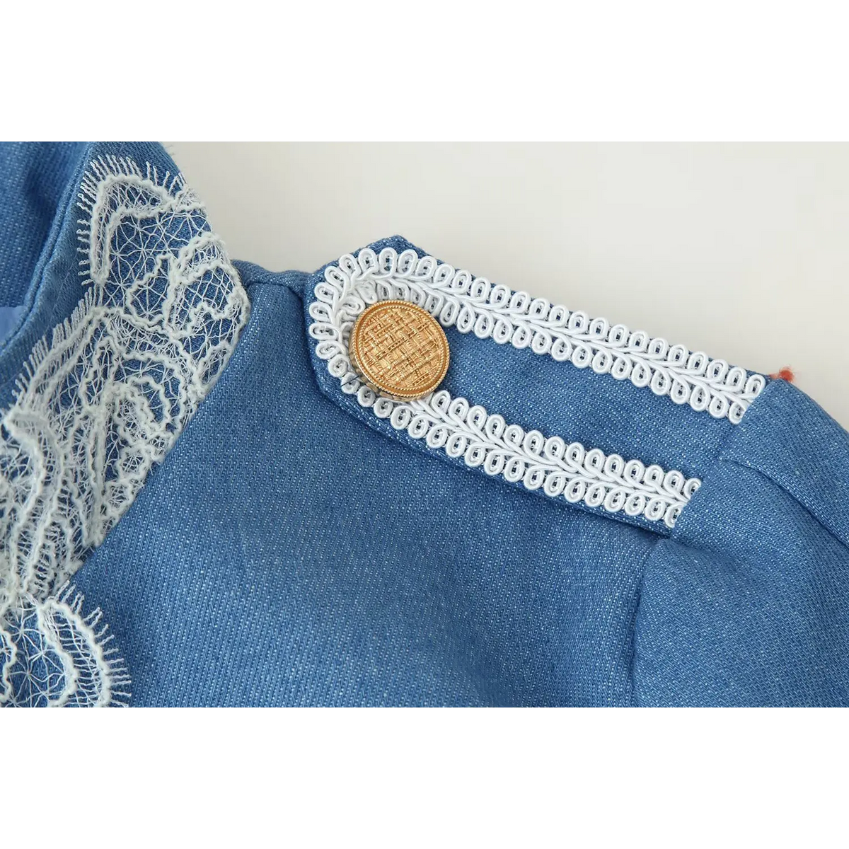 Macro closeup of shoulder epaulet, white braided lace trim and vintage gold round button on blue fabric