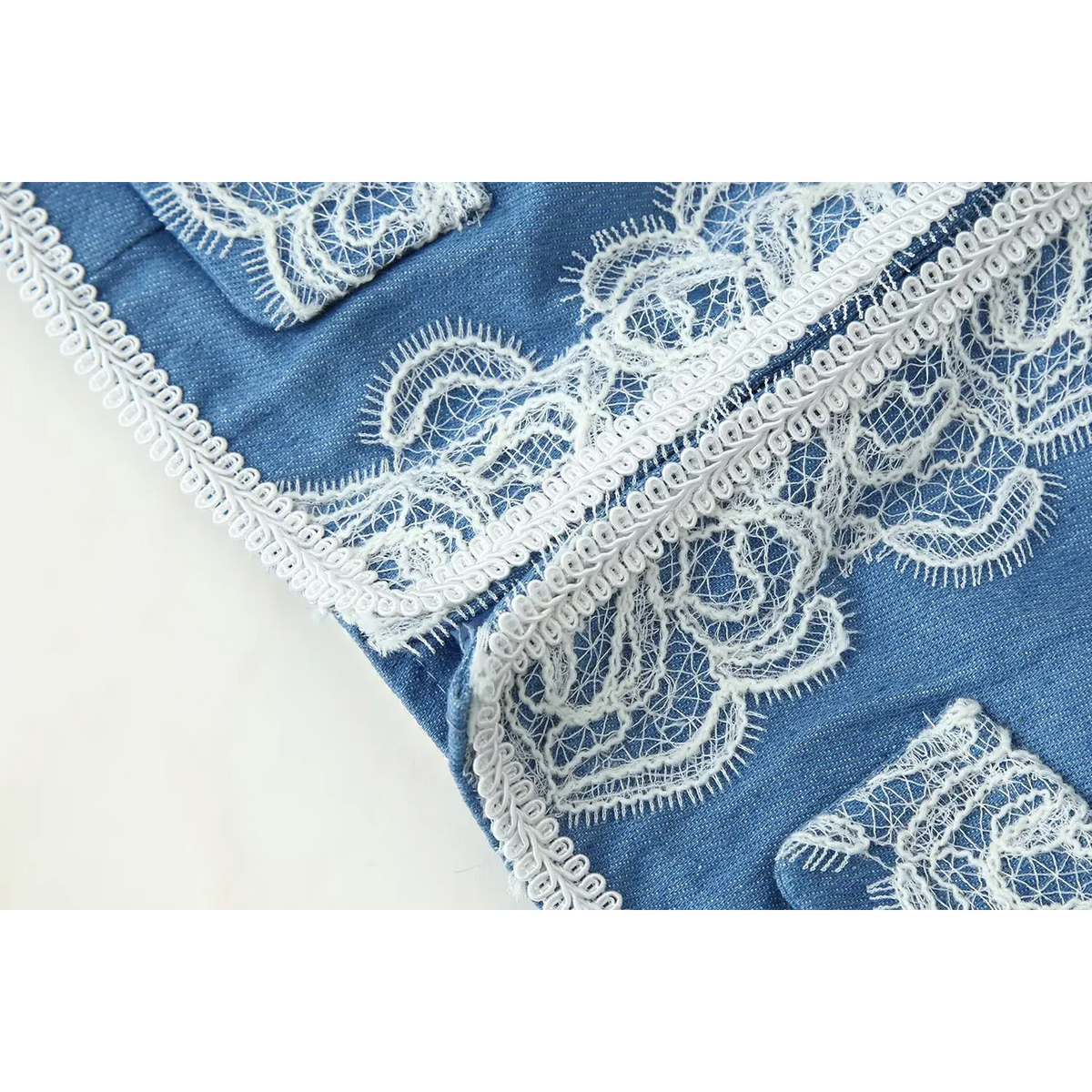Close-up of jacket hem and pocket, ornate white floral lace trim on blue cropped military jacket