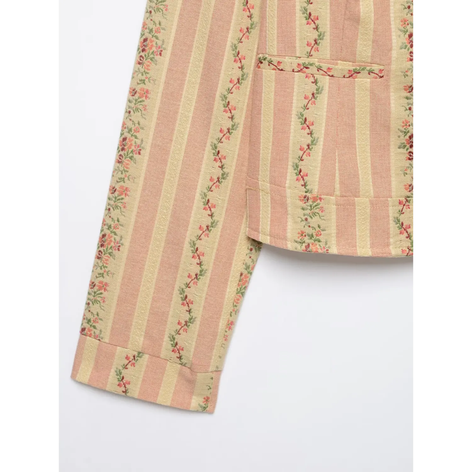 Partial detail view of cropped jacket side patch pocket, long sleeve cuff, floral stripe woven textile