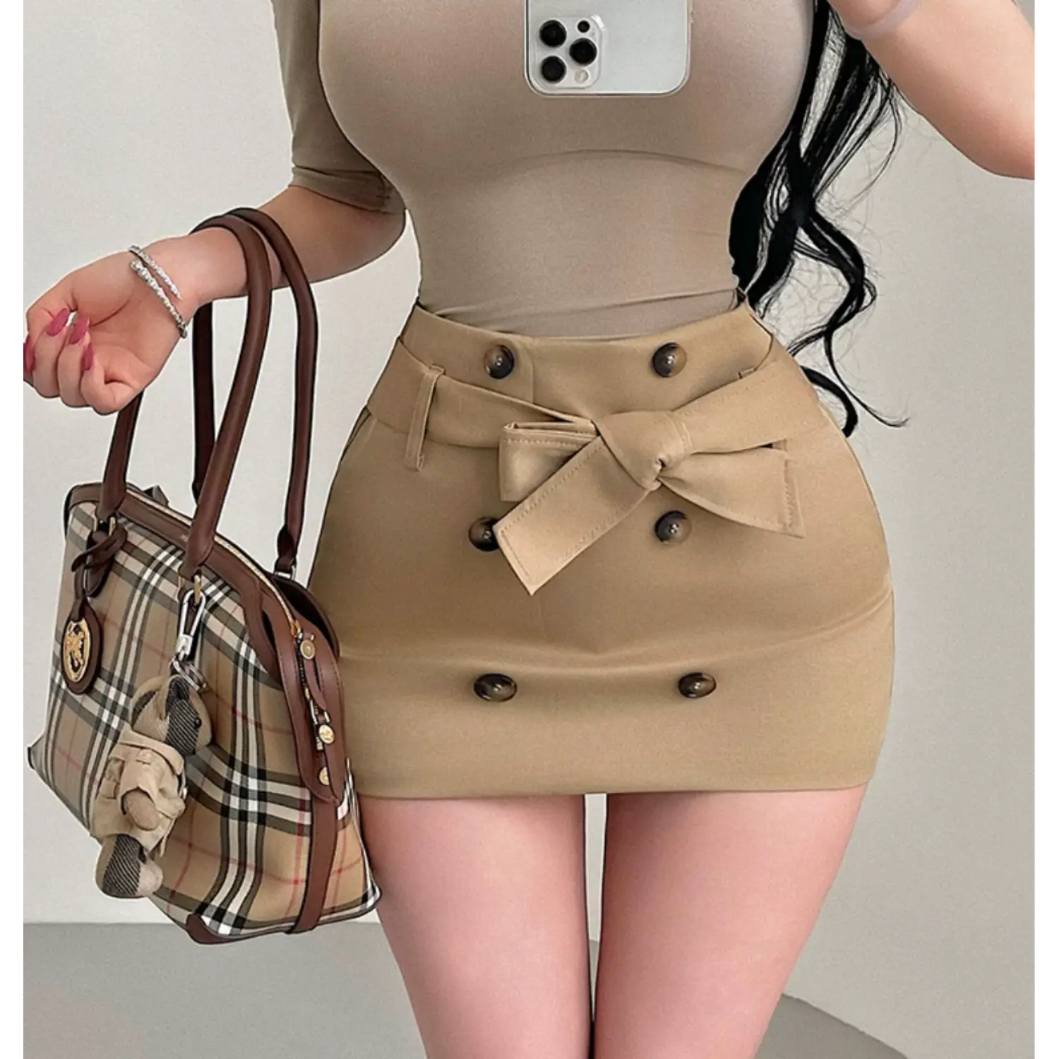 Lifestyle model selfie shot khaki high waist mini skirt, matching fabric bow tie belt, double row dark button detail, slim bodycon silhouette, business casual outfit match with beige short sleeve top