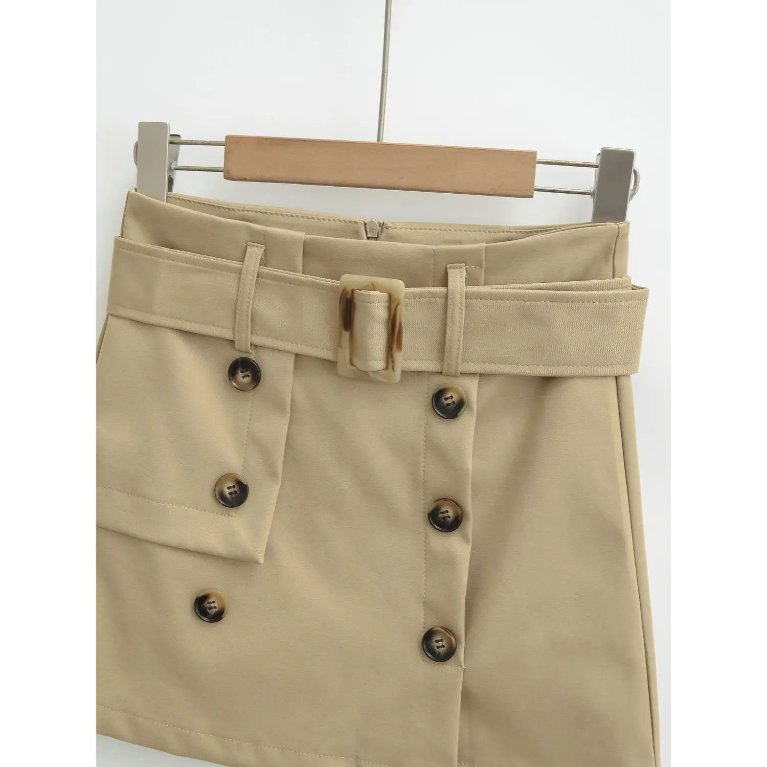 Khaki mini skirt waistband macro flat close-up, tortoise square belt buckle symmetrical horn buttons pocket visible stitching double stitched waist twill fabric white background craft shot