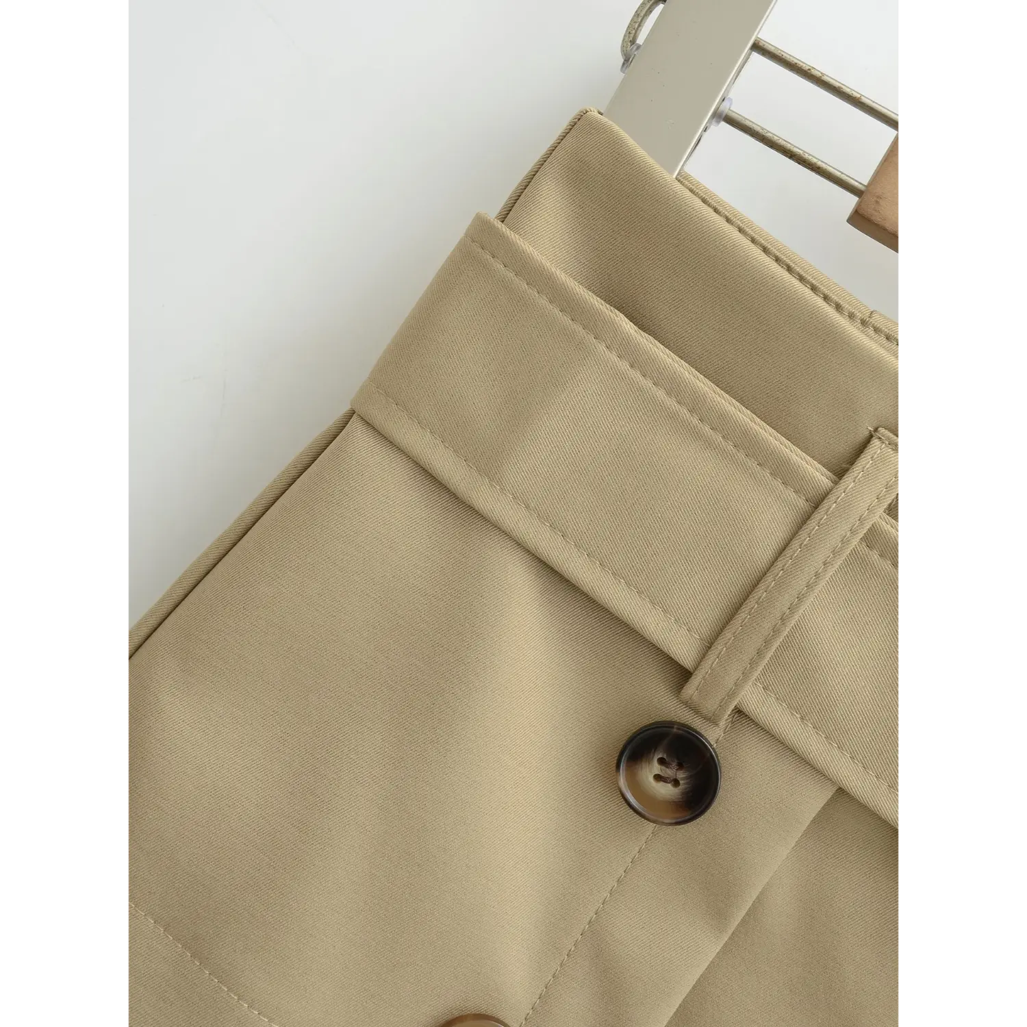 Khaki mini skirt waist belt loop flat close-up, matching fabric symmetrical belt loops even stitching fine twill texture wrinkle-resistant suit fabric white background shot