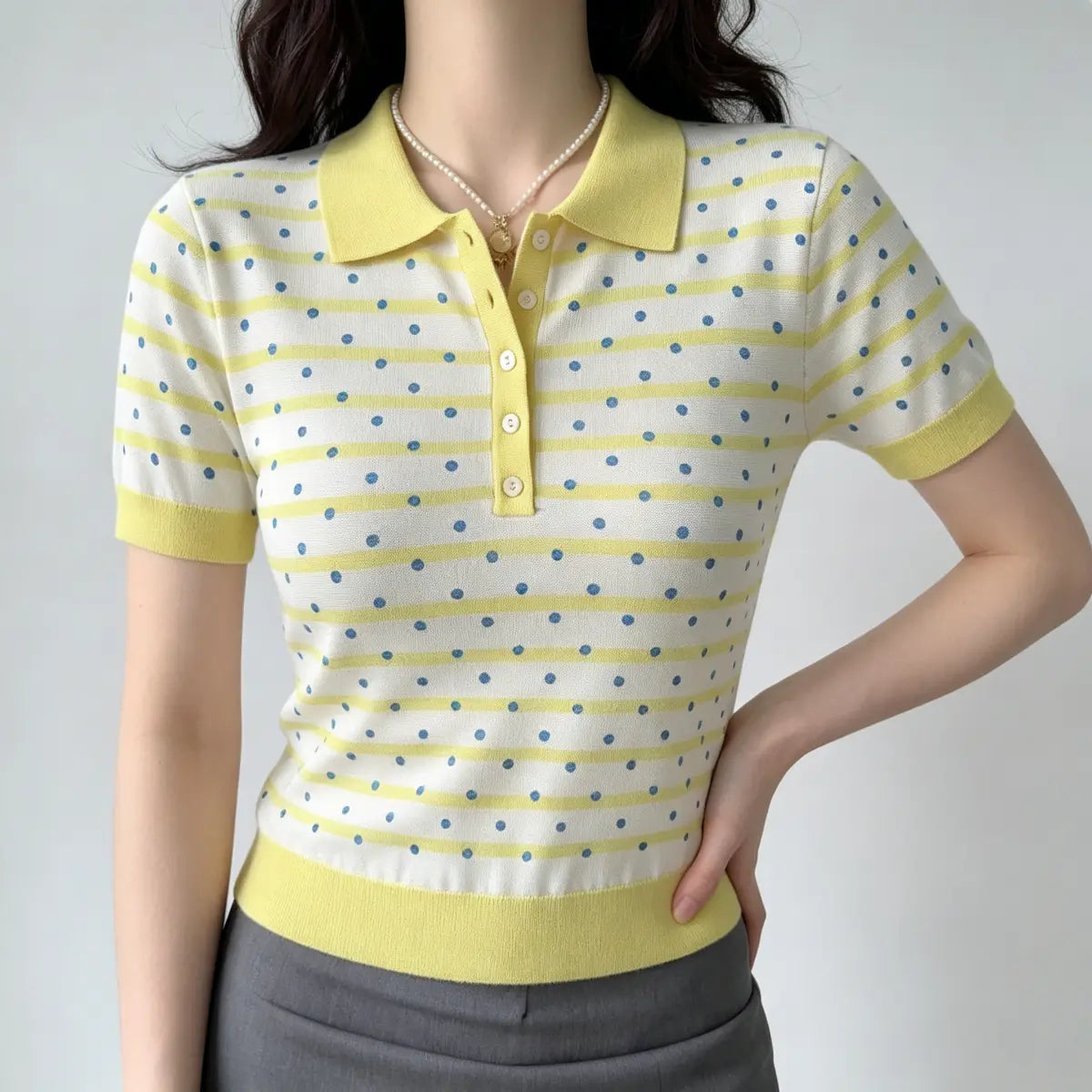 Model with hands on hips, wearing a yellow and white polka dot knit polo shirt, emphasizing the tailored fit and ribbed trim.