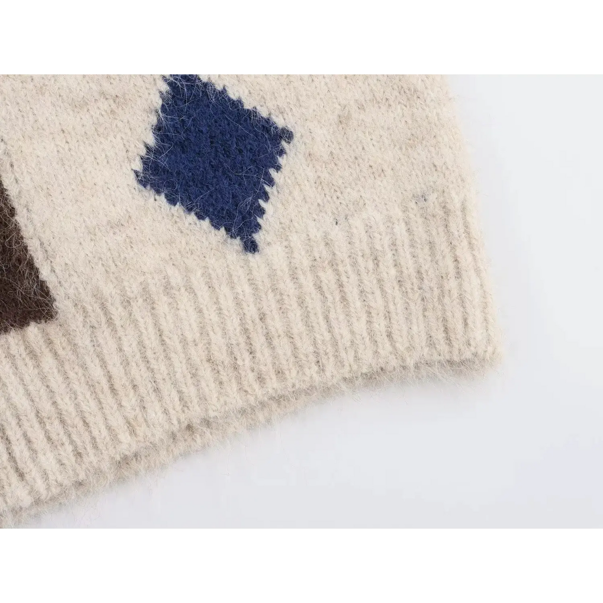 Close-up of ribbed hem and navy diamond argyle pattern of cream fuzzy sweater vest