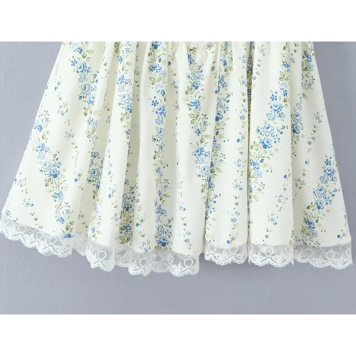 Close-up of the lace hem on a cream floral dress, highlighting the scalloped lace trim and blue floral print.
