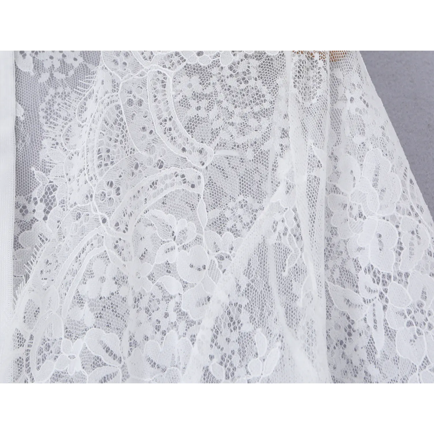Detailed close‑up of ornate floral lace fabric on skirt section of white floor‑length maxi dress