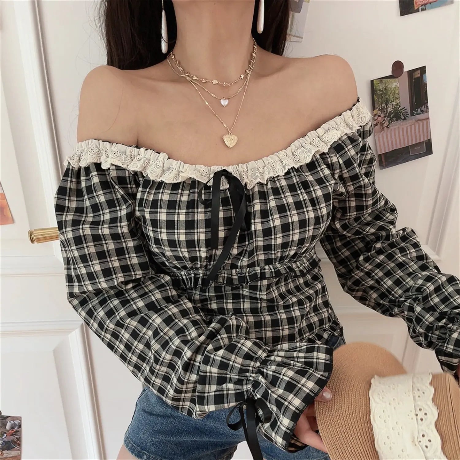 Lace off shoulder gingham crop top low angle close-up model shot, close view neck eyelet lace front black ribbon drawstring waist elastic smocking cuff tie flare sleeve fabric fold texture craft shot