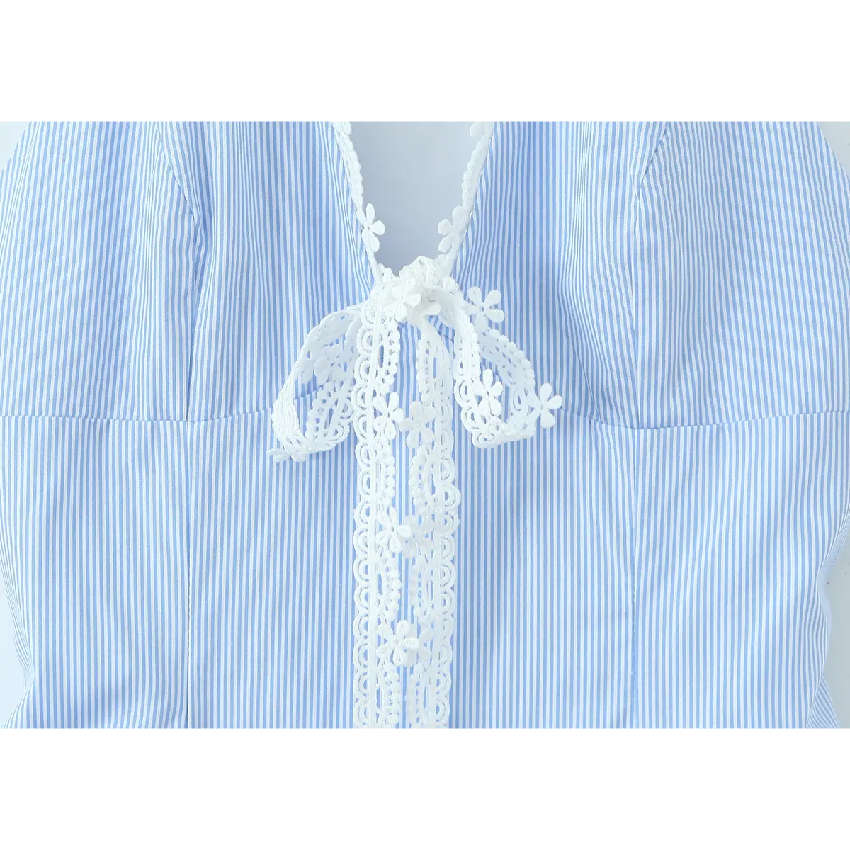 Close-up of the white floral lace tie detail on a blue and white striped halter dress, highlighting the delicate flower patterns.