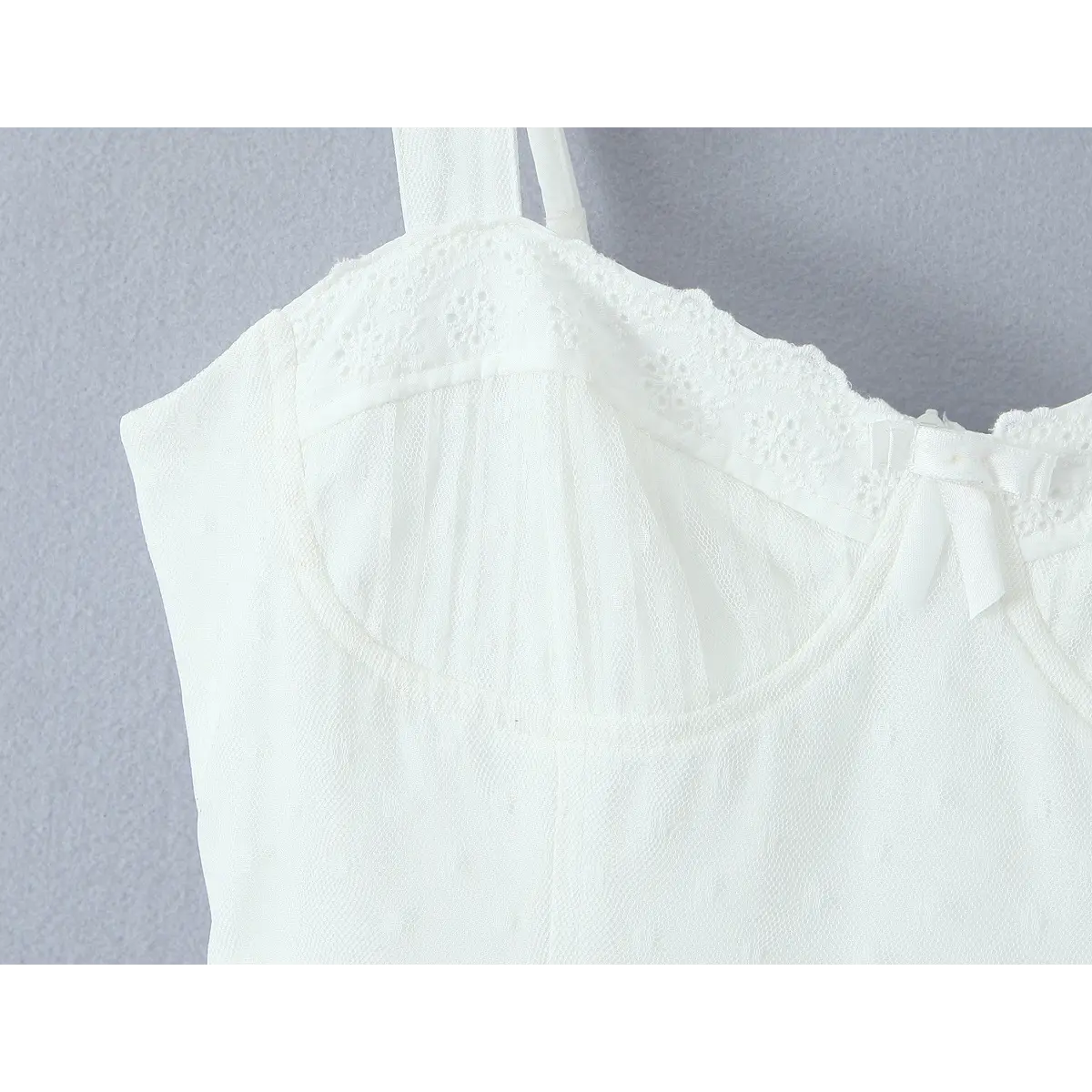Upper bust close-up, eyelet lace scalloped neckline, ruched mesh sweetheart cup and small satin center bow on white corset slip dress.