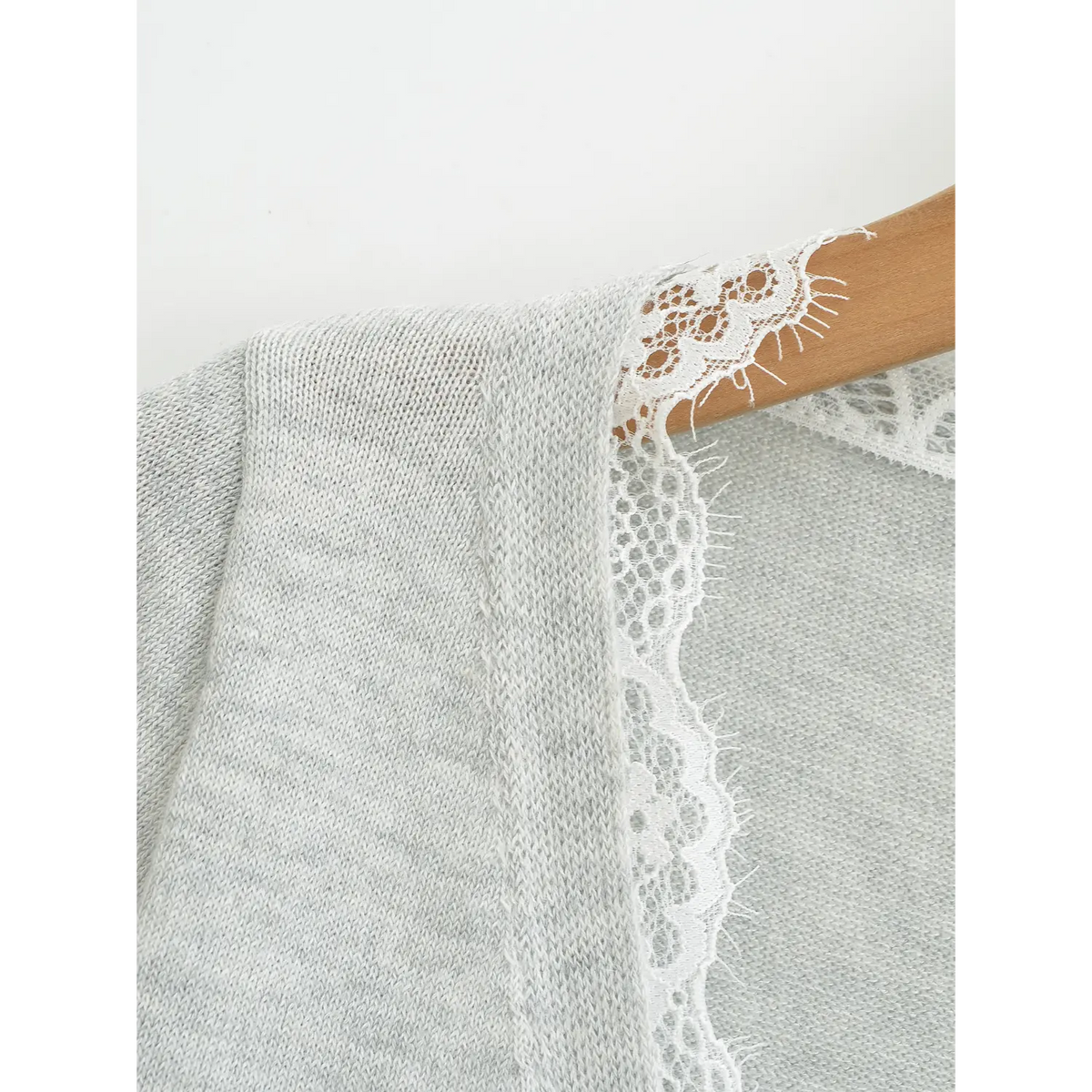 Macro detail view of white frayed eyelash lace on cardigan V neck, soft knit fabric texture