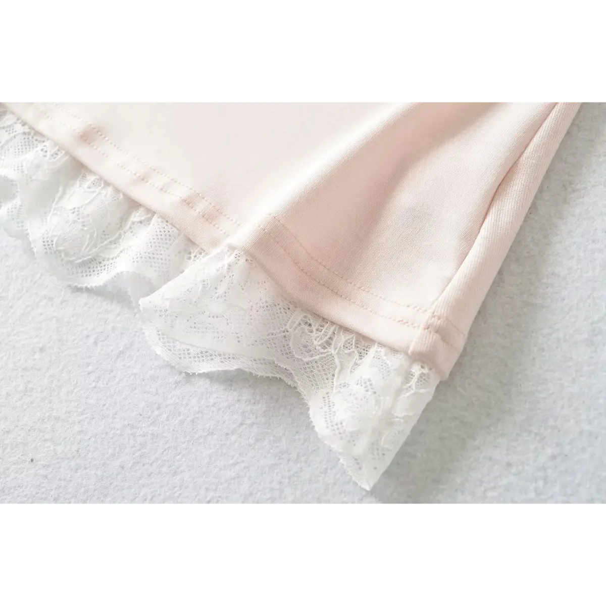 Close-up of the hem corner on a light pink cami top, showing the scalloped lace and stitching details.
